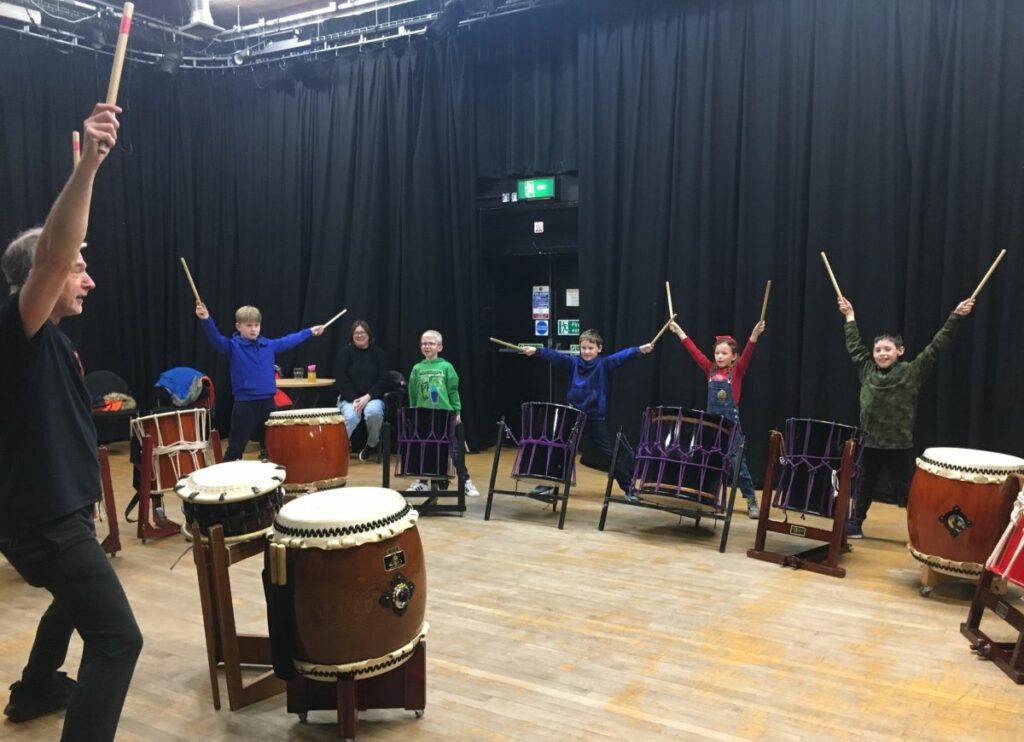 A group of children using large Japanese drums led by a tutor