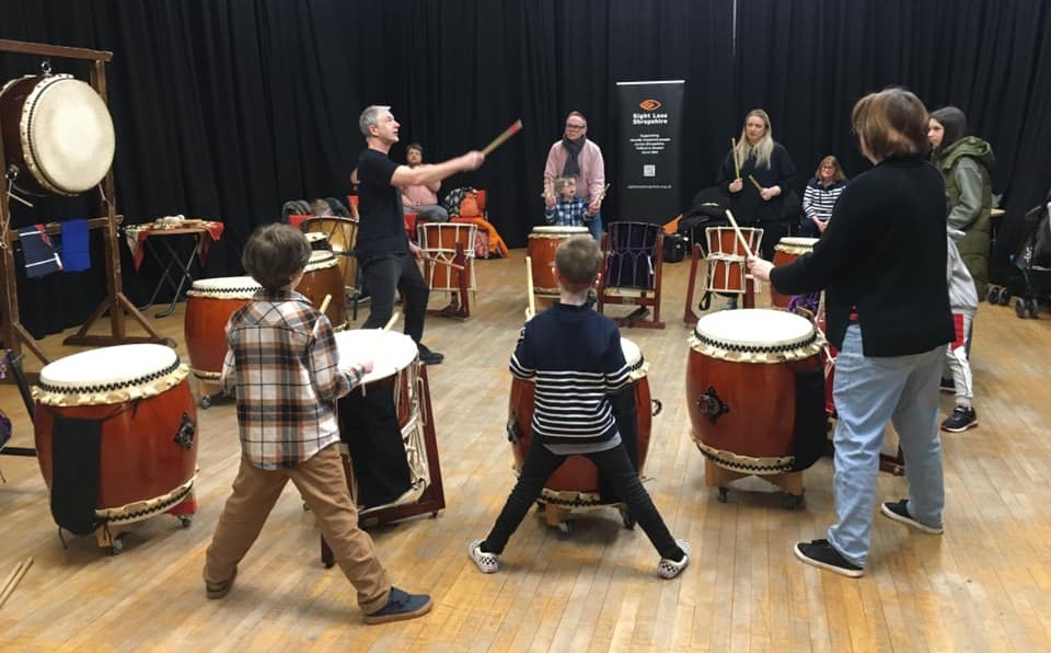 A group of children children using large Japanese drums led by a tutor